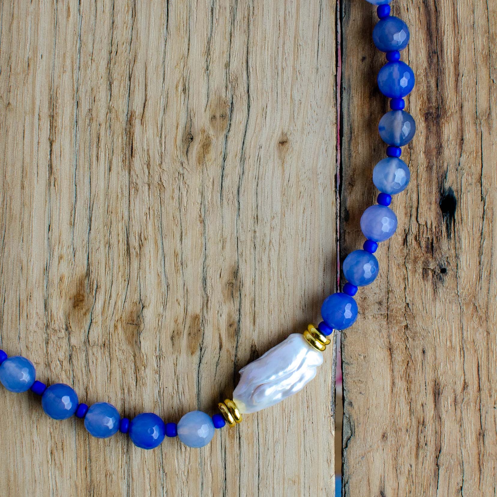 Beaded necklace with a large pearl feature bead on a wooden surface