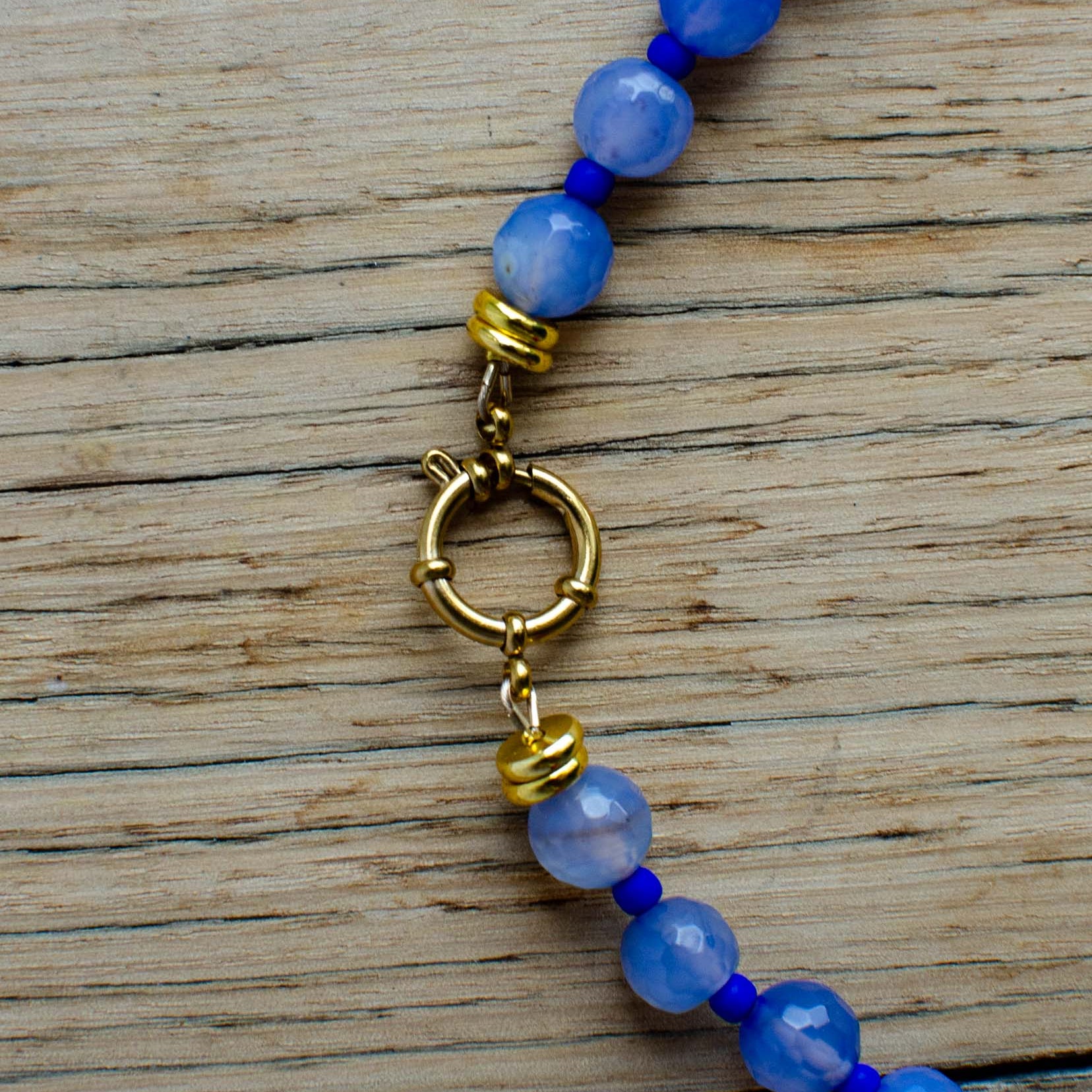 Blue beaded bracelet with a gold clasp on a wooden surface