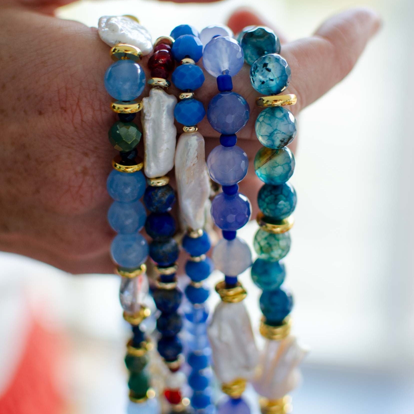 Hand wearing multiple beaded bracelets with blue, green, and gold colors.