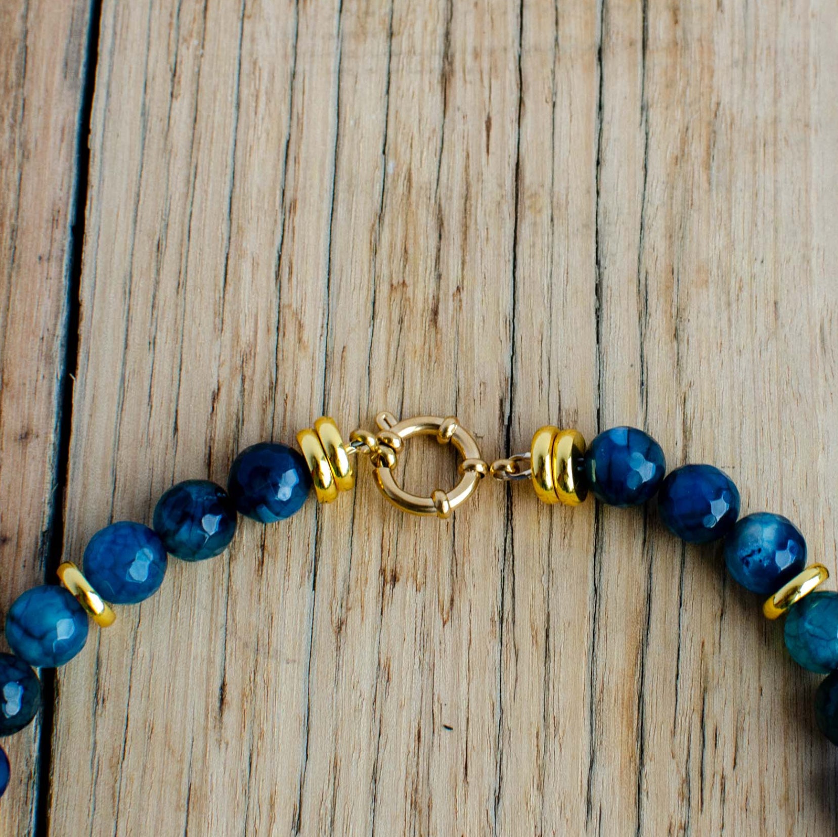 Blue beaded bracelet with gold accents on a wooden surface with bold clasp