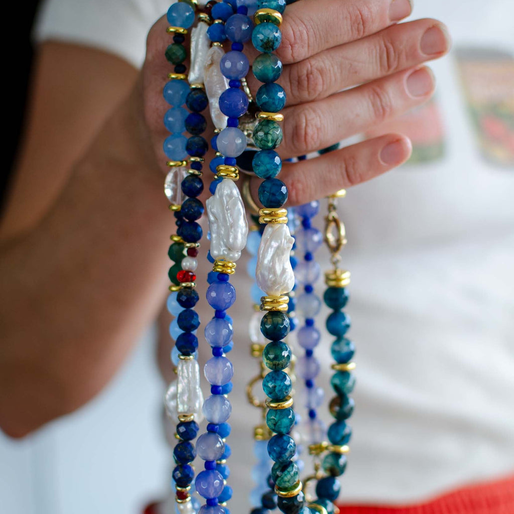 Hand holding multiple colourful beaded necklaces with a blurred background